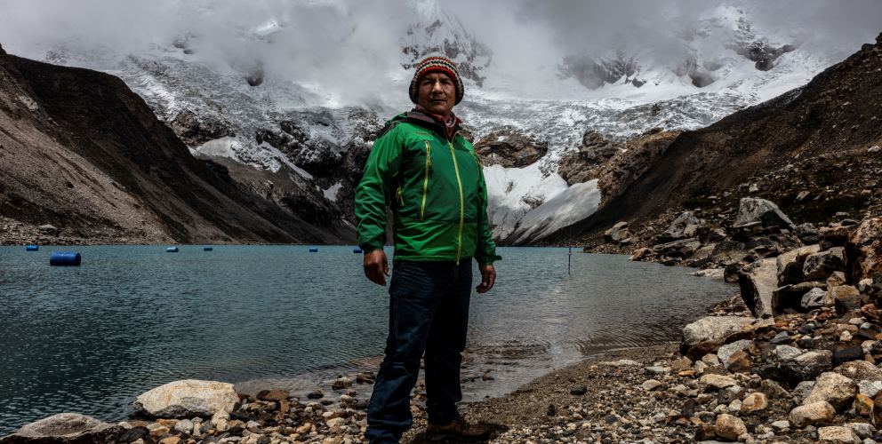 Saúl Luciano Lliuya steht in grüner Jacke vor der Lagune Palcacocha