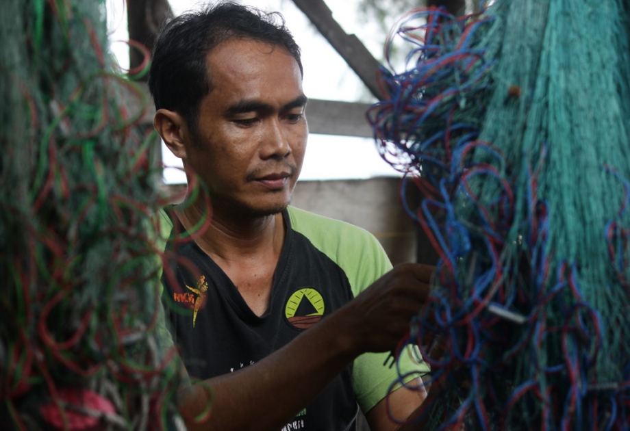 Climate plaintiff Edi from Indonesia mends his fishing net