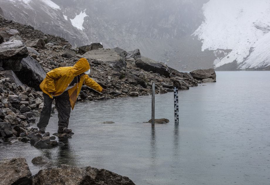 Ein Gletscherseewächter in einer gelben Regenjacke misst den Wasserstand der Lagune