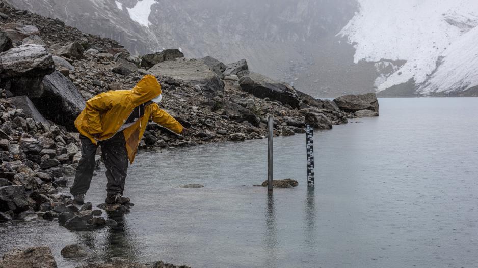 Un guarda del lago glaciar con chubasquero amarillo mide el nivel del agua de la laguna